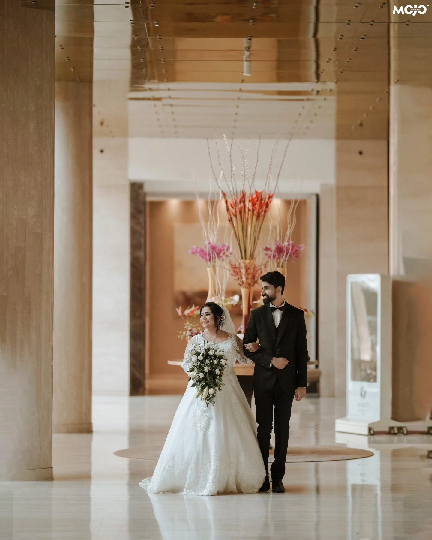 A newlywed couple walking together through a bright hotel lobby